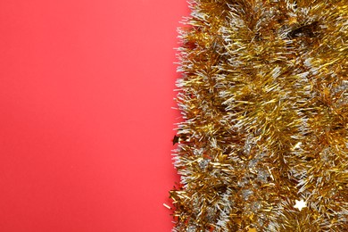 Photo of Shiny golden tinsel on red background, top view. Space for text