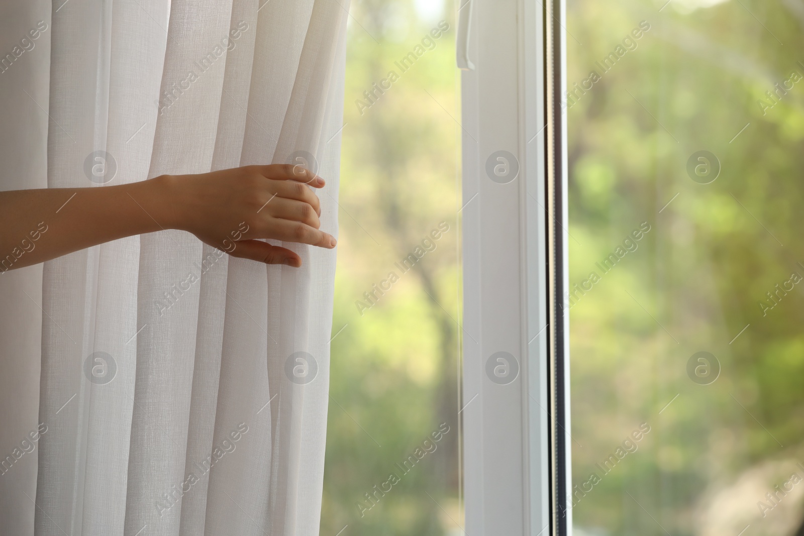 Photo of Woman opening white window curtains in room, closeup. Space for text