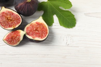 Photo of Whole and cut ripe figs with leaf on white wooden table, flat lay. Space for text
