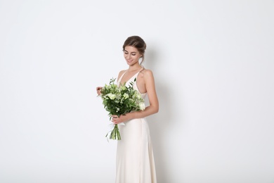 Young bride wearing wedding dress with beautiful bouquet on light background