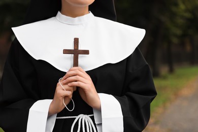 Young nun with Christian cross in park outdoors, closeup