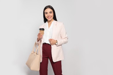 Photo of Young woman with stylish bag and cup of hot drink on white background