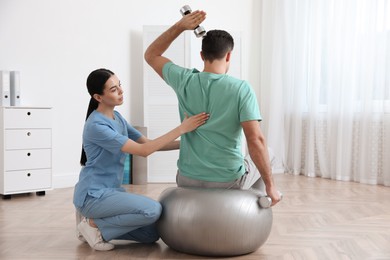 Photo of Orthopedist helping patient to do exercise with dumbbells in clinic. Scoliosis treatment