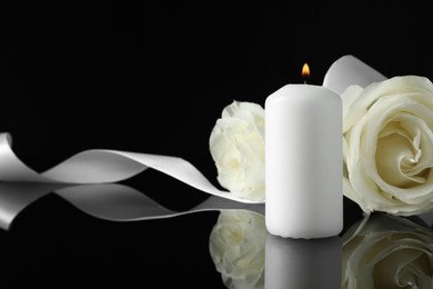 Photo of Burning candle, white roses and ribbon on black mirror surface in darkness, closeup with space for text. Funeral symbols