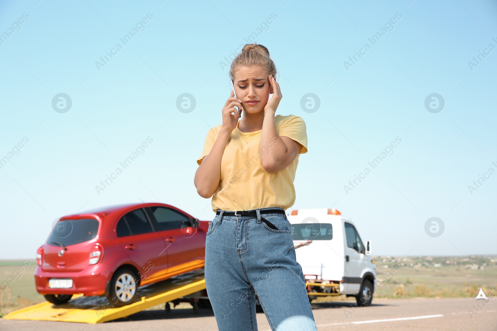 Photo of Woman talking on phone near tow truck with broken car outdoors