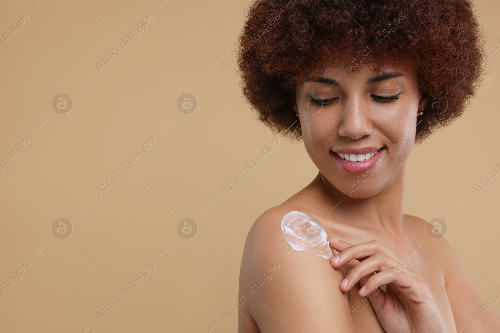 Photo of Beautiful young woman applying body cream onto shoulder on beige background, space for text