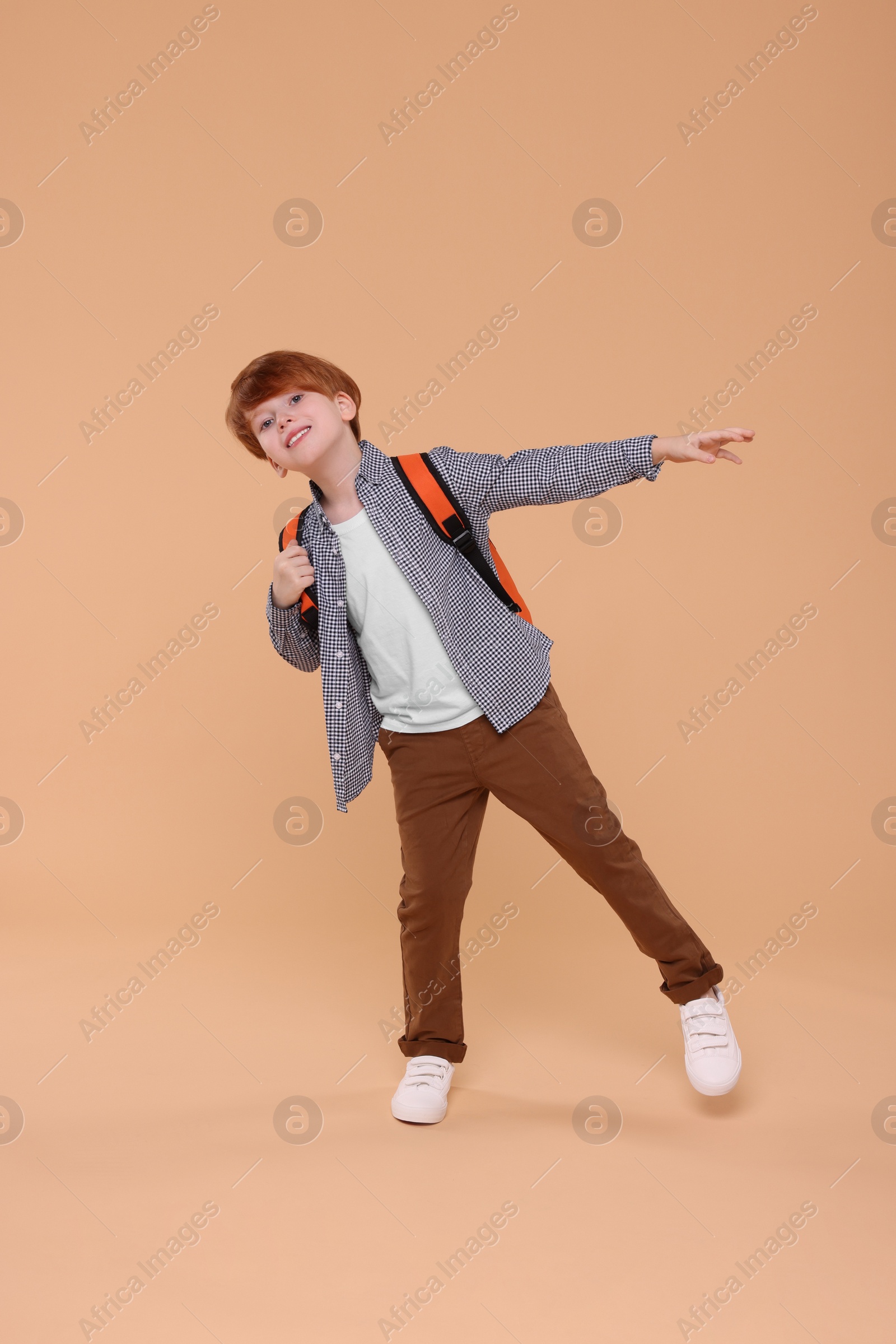 Photo of Happy schoolboy with backpack having fun on beige background