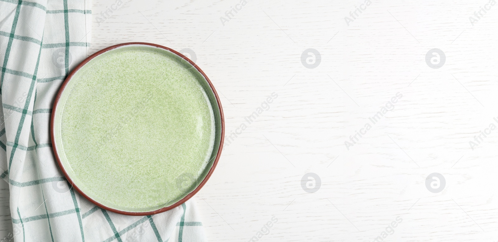 Photo of Empty light green plate and fabric on white wooden table, flat lay. Space for text