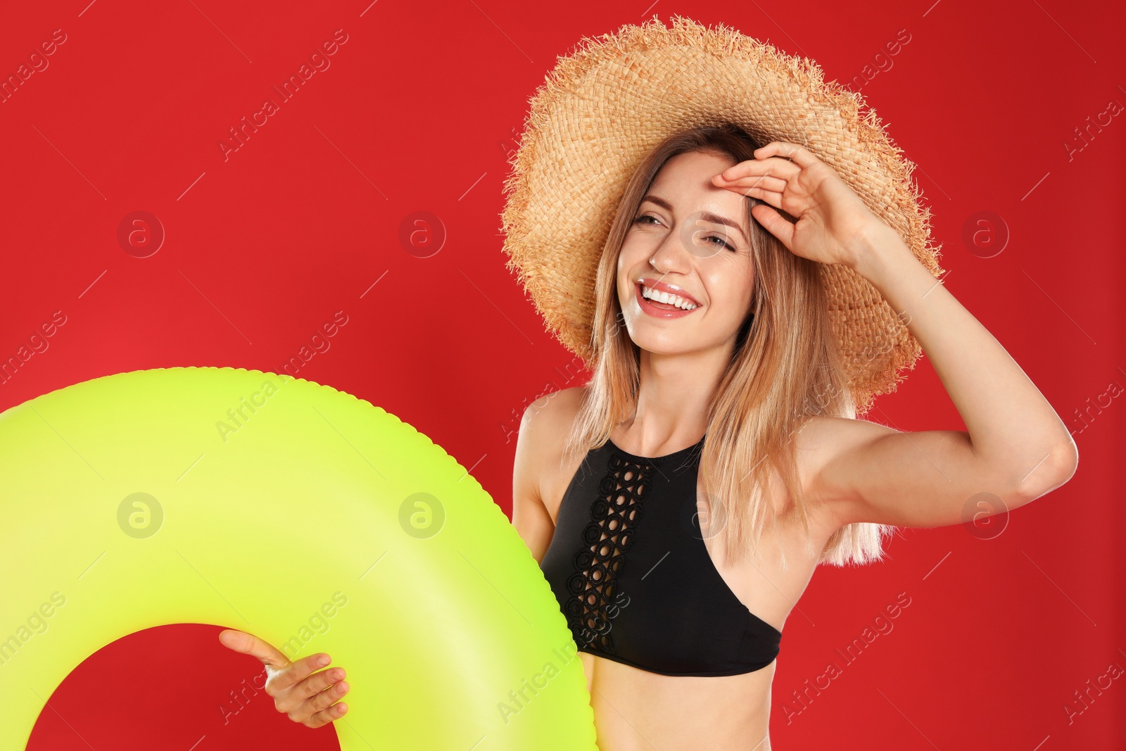 Photo of Beautiful young woman in stylish bikini with yellow inflatable ring on red background