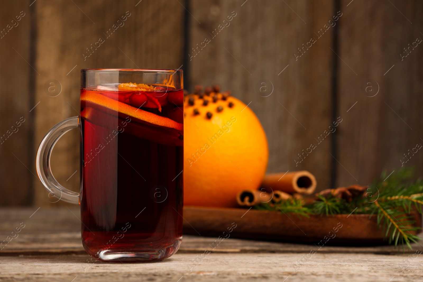 Photo of Aromatic mulled wine in glass cup on wooden table, space for text