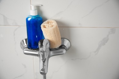 Natural loofah sponge and shower gel bottle on faucet in bathroom. Space for text