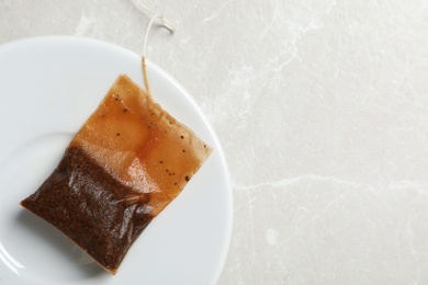 Photo of Saucer with used tea bag on light grey table, top view. Space for text