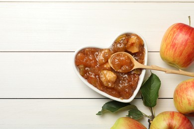 Photo of Tasty apple jam in bowl and fresh fruits on white wooden table, flat lay. Space for text