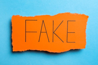 Photo of Orange paper piece with word FAKE on light blue background, top view