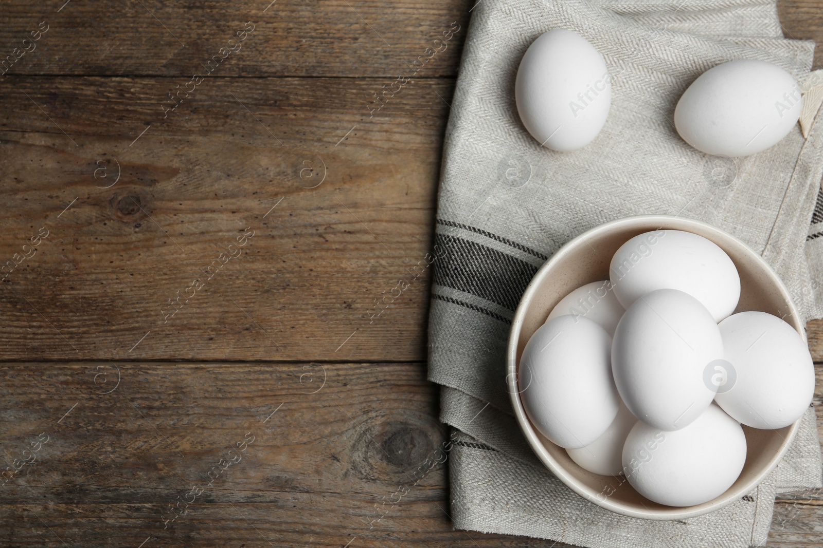 Photo of Many fresh raw chicken eggs in bowl on wooden table, flat lay. Space for text