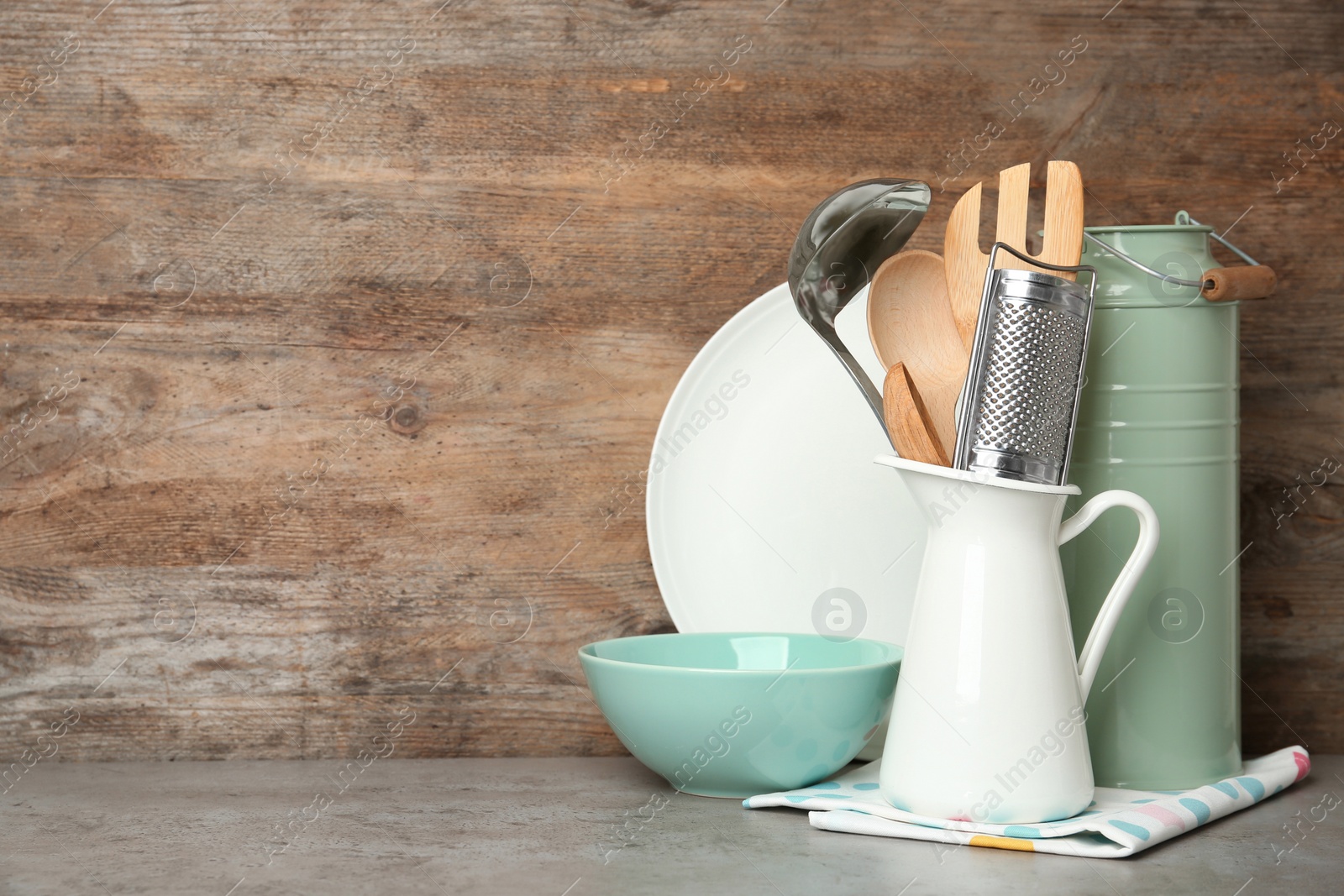 Photo of Different kitchen utensils on grey table against wooden background. Space for text