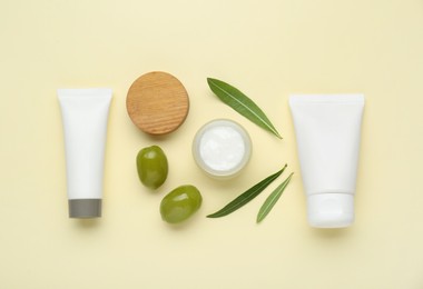 Cosmetic products with olive essential oil on beige background, flat lay