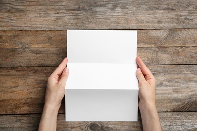 Photo of Young woman holding blank brochure at wooden table, top view. Mock up for design