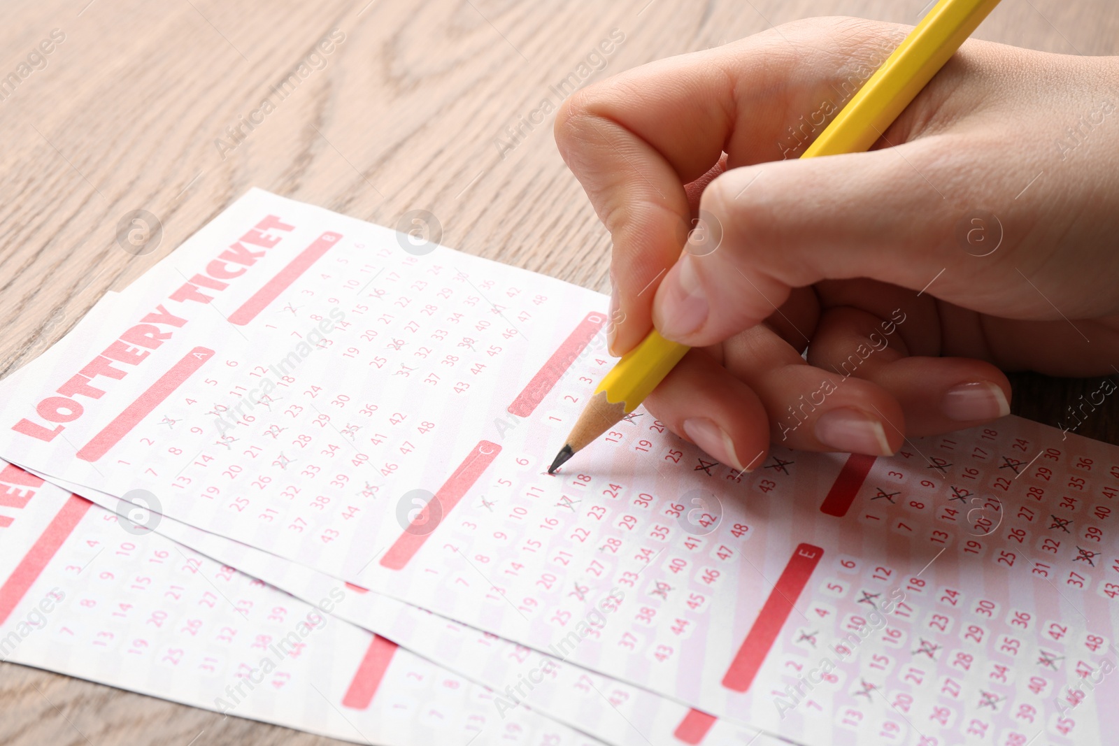 Photo of Woman filling out lottery tickets with pencil on wooden table, closeup. Space for text