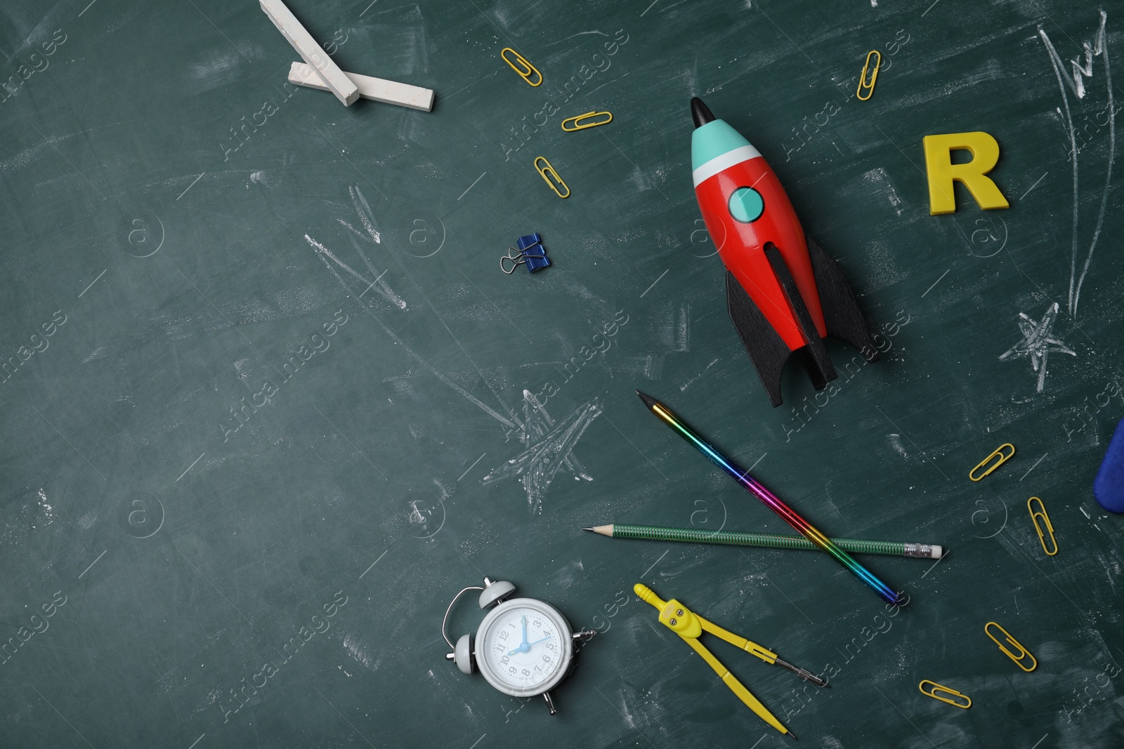 Photo of Bright toy rocket, school supplies and drawings on chalkboard, flat lay. Space for text