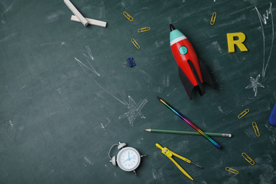 Photo of Bright toy rocket, school supplies and drawings on chalkboard, flat lay. Space for text