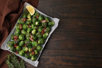 Photo of Delicious roasted Brussels sprouts, bacon, lemon and rosemary on wooden table, top view. Space for text