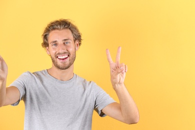 Handsome young man laughing and taking selfie on color background