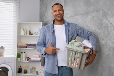 Photo of Happy man with basket full of laundry in bathroom