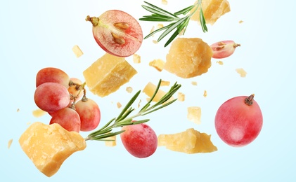 Pieces of delicious parmesan, grapes and rosemary falling on light blue background