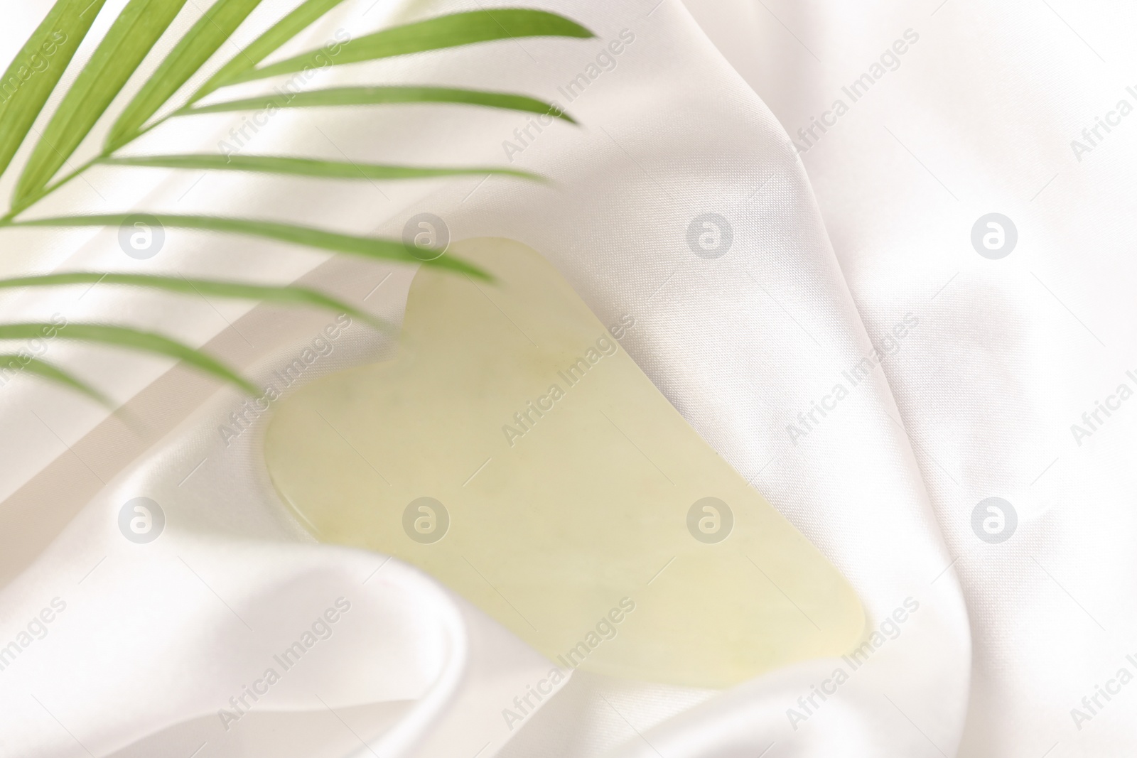 Photo of Jade gua sha tool and green leaf on white fabric, above view