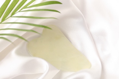 Jade gua sha tool and green leaf on white fabric, above view