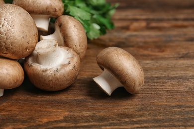 Photo of Fresh champignon mushrooms on wooden background, space for text