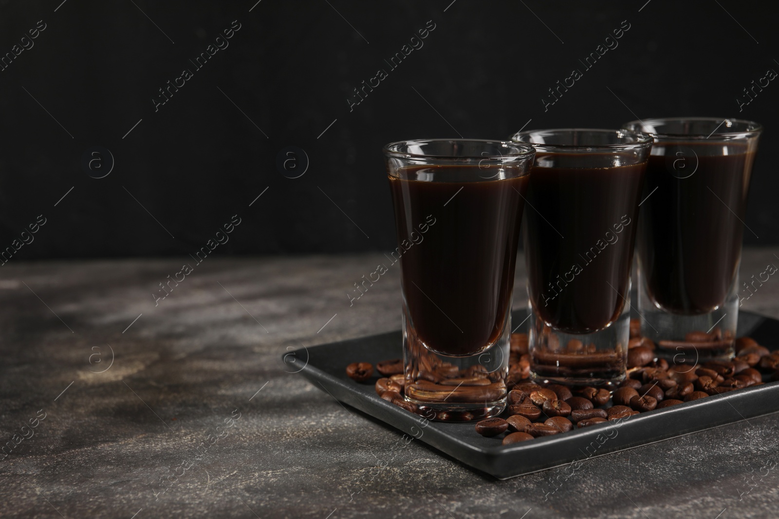 Photo of Shot glasses with coffee liqueur and beans on grey textured table, space for text