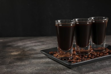 Photo of Shot glasses with coffee liqueur and beans on grey textured table, space for text