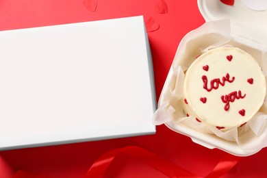 Photo of Tasty bento cake with Love You inscription in takeaway packaging and box on red table, flat lay