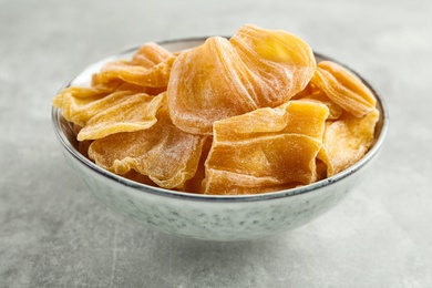 Photo of Delicious dried jackfruit slices in bowl on light grey table, closeup