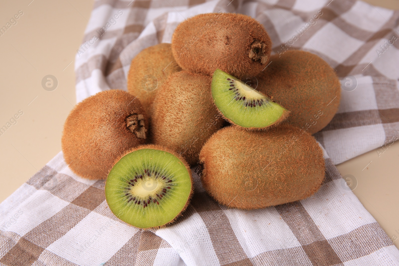 Photo of Heap of whole and cut fresh kiwis on beige table