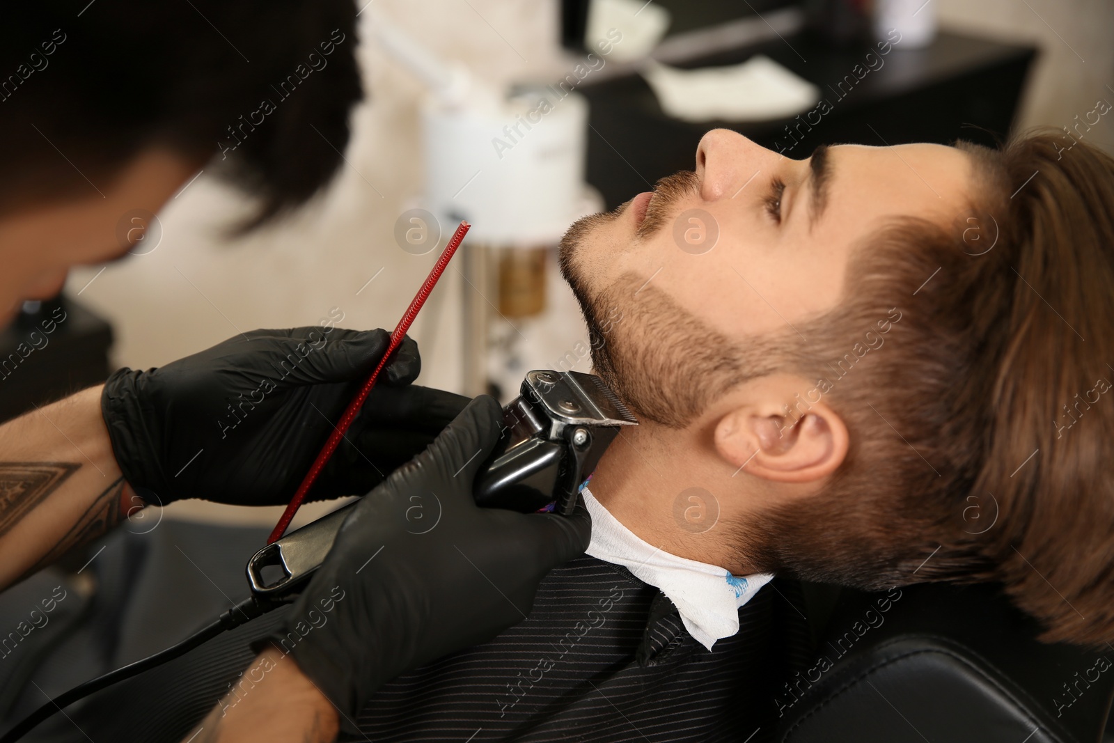 Photo of Hairdresser trimming client's beard in barbershop. Professional shaving service