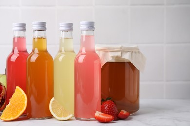 Delicious kombucha in glass bottles, jar and fresh fruits on white marble table