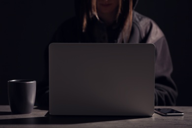 Photo of Woman with laptop and smartphone at table in darkness, closeup