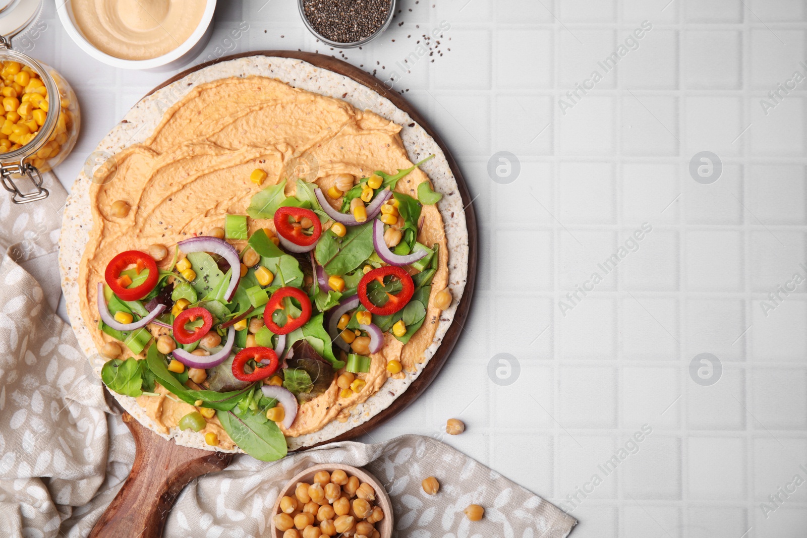 Photo of Tortilla with hummus and vegetables on white table, flat lay. Space for text