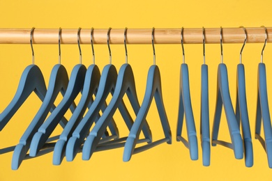 Wooden rack with clothes hangers on color background