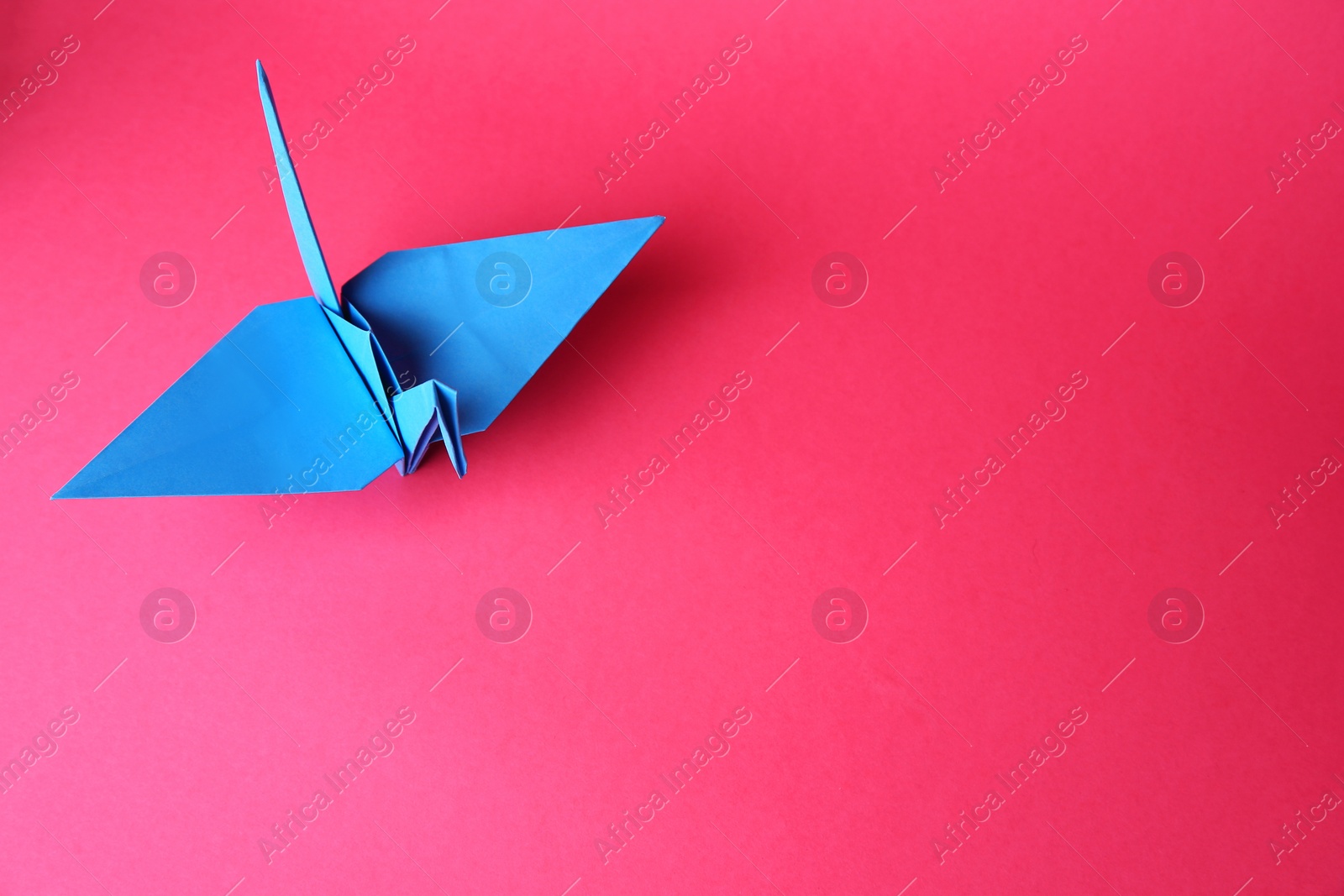 Photo of Origami art. Handmade paper crane on pink background, above view. Space for text