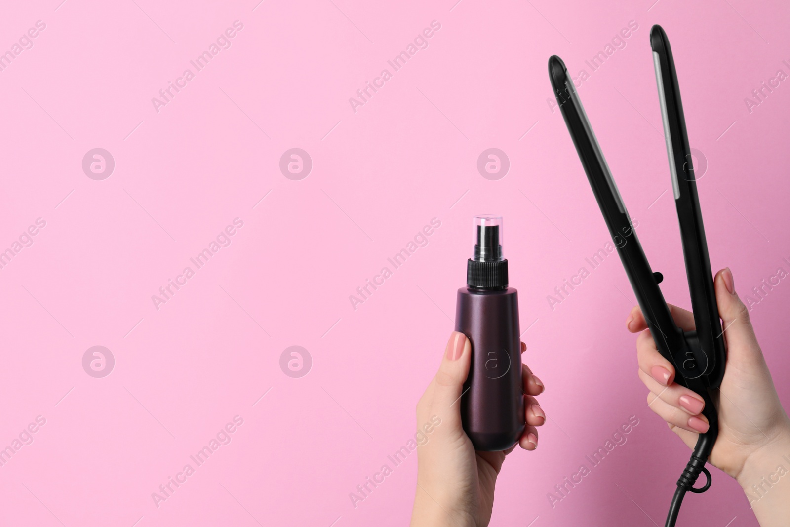 Photo of Woman holding spray bottle with thermal protection and stylish straightener on light pink background, closeup. Space for text