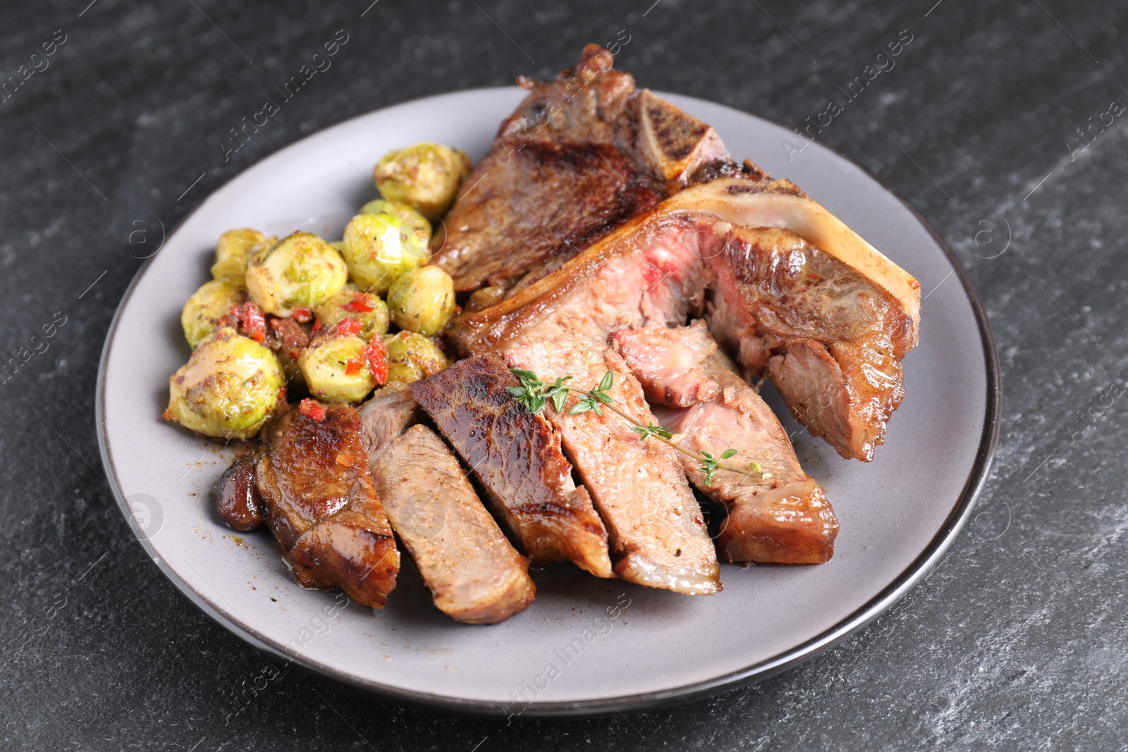 Photo of Delicious fried beef meat, vegetables and thyme on black table, closeup