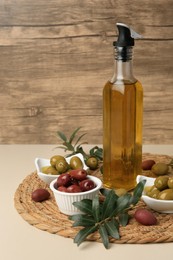 Photo of Bottle of oil, olives and tree twigs on beige table