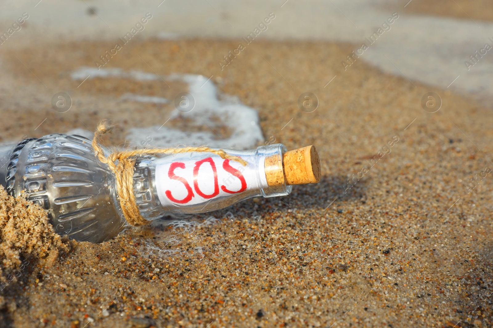 Photo of Glass bottle with SOS message on sand near sea