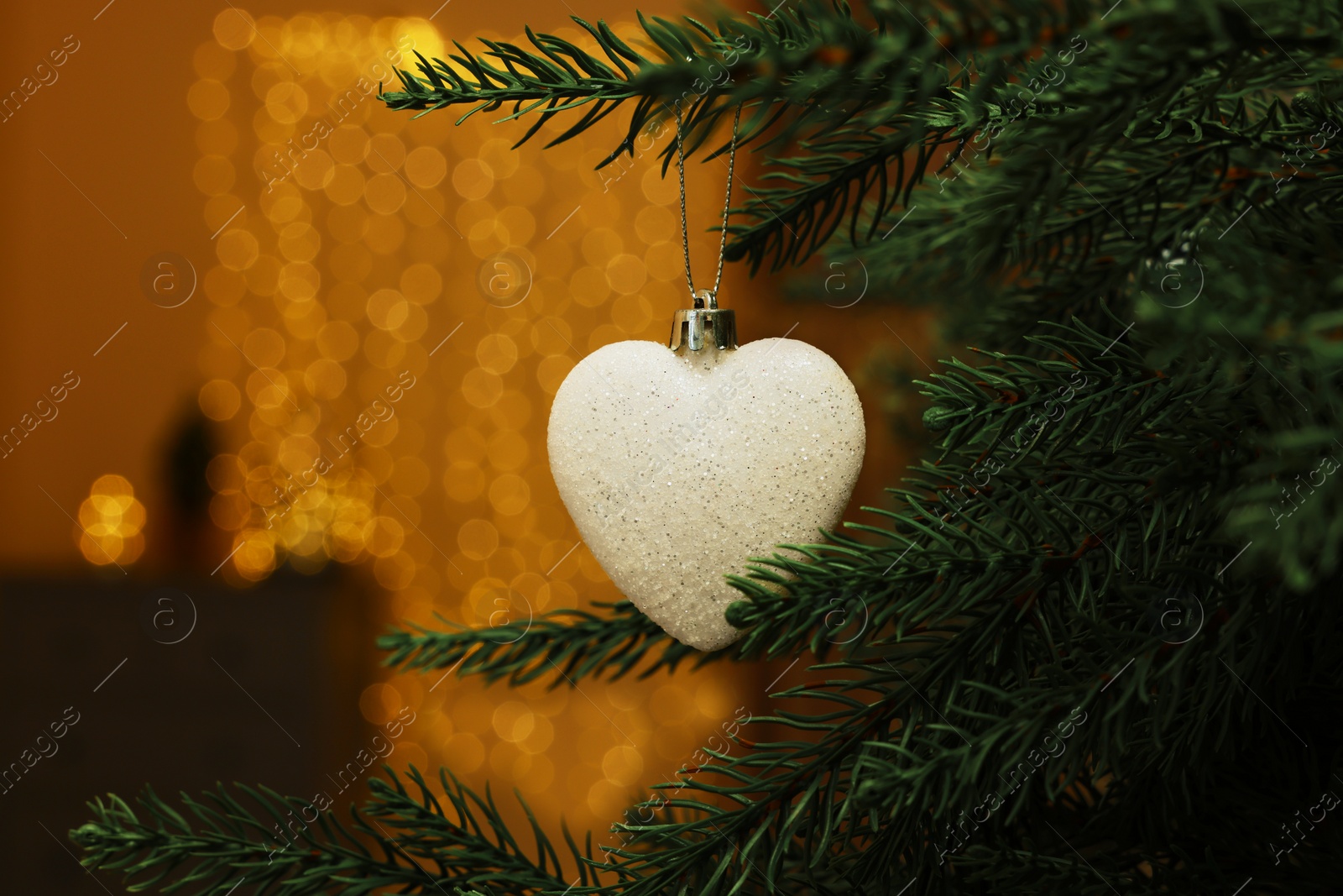 Photo of Beautiful bauble in shape of heart hanging on Christmas tree indoors, closeup. Space for text