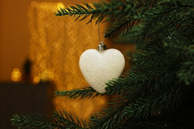 Photo of Beautiful bauble in shape of heart hanging on Christmas tree indoors, closeup. Space for text