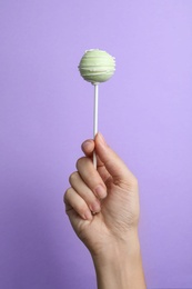 Photo of Woman holding sweet cake pop on lilac background, closeup